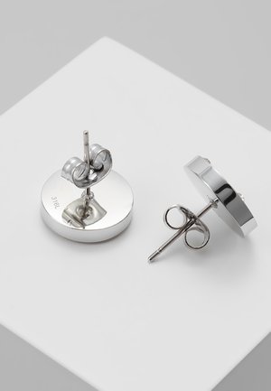 Deux clous d'oreilles ronds en acier inoxydable argenté avec attache papillon sur une surface blanche.