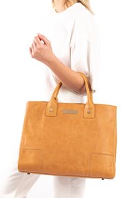 Tan leather tote bag with stitched accents, two top handles, and a metallic embellishment on the front. Smooth texture and rectangular shape.