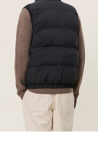 Svart pufferväst med horisontell quiltning, elastisk nederkant, bärs över en brun ribbad tröja, tillsammans med krämfärgade kordflodbyxor.