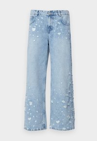 Jeans de mezclilla de tiro ancho en azul claro, con parches desgastados y bordes deshilachados, que cuentan con cinco bolsillos y un cierre frontal de botones.