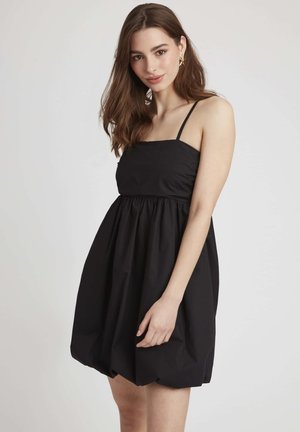 Robe noire sans manches avec un corsage ajusté et une jupe volumineuse, fabriquée en tissu léger, dotée de fines bretelles spaghetti et d'un design froncé.