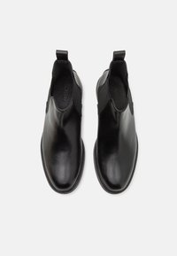 Botas de tobillo de piel negra con paneles laterales elásticos y tiradores. Textura suave y diseño de punta redondeada. Suela de goma resistente.