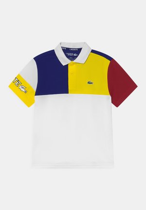 Koszulka polo z krótkim rękawem, białym kołnierzykiem, blokami kolorów: niebieskim, żółtym, białym i czerwonym, z logo Lacoste na piersi i rękawie.