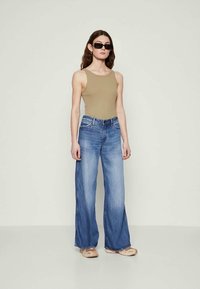 Wide-leg blue jeans with a faded finish, paired with a sleeveless beige top and neutral sandals. Sunglasses complete the look.