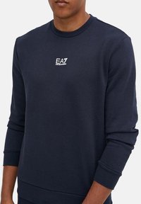 Felpa blu navy realizzata in morbido misto cotone, con collo a giro, polsini a coste e un piccolo logo EA7 bianco sul petto.