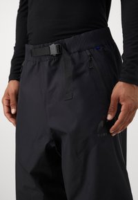 Crne vodootporne skijaške hlače s fleksibilnim pojasom, podesivim remenom, džepom sa patentnim zatvaračem i logo detaljima na bedru.