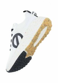 Witte sportieve schoen met zwart circulair logo, zwarte zool op de neus en een gestructureerde beige zool met kleurrijke spikkels.