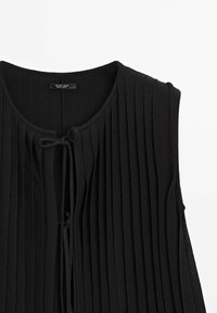 Haut noir sans manches en maille côtelée avec encolure ronde et fermeture à nouer devant, design minimaliste, rayures verticales texturées.