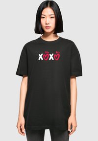 Tricou din bumbac negru, cu un grafic frontal ce prezintă textul "XOXO" în alb și roșu, alături de desene cu inimi, într-un croi relaxat.
