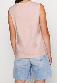 Top in cotone rosa senza maniche con scollo rotondo, texture liscia e una forma leggermente aderente, abbinato a pantaloni corti in denim blu chiaro.