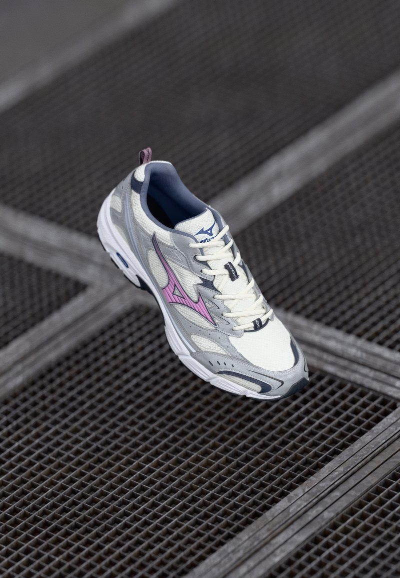 White and gray athletic shoe with pink accents, mesh upper, textured sole, and lace-up front. Features a logo and a pull tab at the heel.