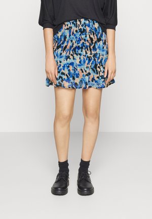 Mujer con una minifalda de patrón azul, negro y melocotón, medias negras y zapatos negros con cordones, sobre un fondo liso.