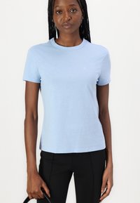 T-shirt en coton bleu clair à manches courtes, décolleté rond, et petit logo sur la poitrine ; assorti avec un pantalon noir. Texture lisse.