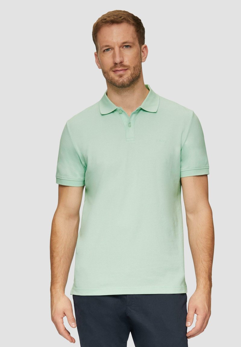 Jasnozielona koszulka polo z bawełny, z klasycznym kołnierzykiem, krótkimi rękawami i subtelnym logo na piersi, w zestawie z ciemnymi spodniami.