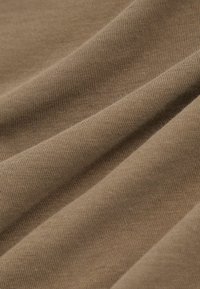 Kokvilnas audums klusā bēša tonī ar gludu tekstūru un smalku rievotu rakstu, noklāts tā, lai izceltu dziļumu un locījumus.