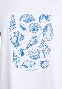 White t-shirt featuring a blue shell print, including various shell types and a "SALTY" text at the bottom. The design is detailed and intricate.