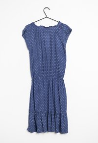 Sininen mekko, jossa on valkoisia pilkkuja, lyhyet hihat, joustava vyötärö, poimutettu helma ja pieni punainen yksityiskohta olkapään lähellä.