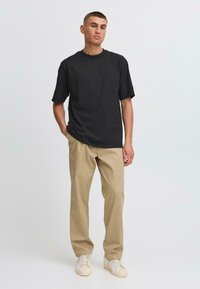 T-shirt noir en coton, coupe décontractée, manches courtes. Associé à un pantalon en coton beige et des baskets blanches avec des détails texturés.