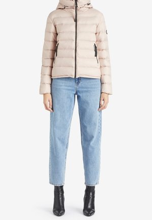 Femme portant une doudoune rose clair matelassée avec capuche, un jean droit bleu clair et des bottines noires.