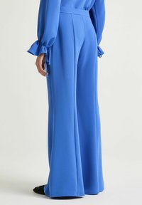 Pantaloni blu a gamba larga in tessuto liscio con vita alta e pieghe sottili, con dettagli a fiocco sulle maniche di una maglia coordinata.