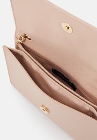 Portefeuille beige clair au toucher lisse, avec une fermeture à bouton pression en ton doré, une poche intérieure et une étiquette à l'intérieur qui indique "ANNA FIELD."