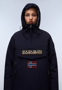 Navy blue insulated parka with a high collar, front pouch, zippered side pocket, and embroidered brand logo and Norwegian flag patch.