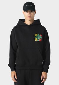 Sudadera negra hecha de tela suave, con un bolsillo frontal y un colorido patrón de hojas en el lado izquierdo del pecho. Incluye un dobladillo y puños acanalados.