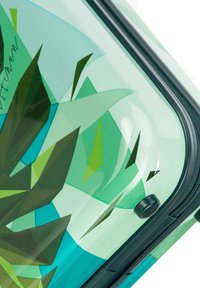 Valigia rigida con un design trasparente verde-blu caratterizzato da motivi geometrici a forma di foglia e un dettaglio con cerniera nera.