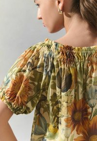 Blusa floral con escote fruncido y mangas abullonadas. Fabricada en un tejido ligero con estampados de flores en naranja, amarillo y verde.