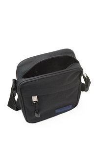 Bolso cruzado de tela negra con un compartimento principal con cremallera y un bolsillo frontal. Cuenta con una correa ajustable y una superficie texturizada con detalles de logo.