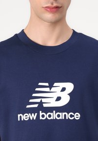 Sötétkék pamut póló, nagy fehér "new balance" logóval, stilizált betűkkel, kerek dekoltázzsal és rövid ujjakkal.