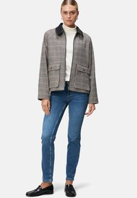 Houndstooth-gepatroneerde jas met een zwarte kraag, twee voorzakken, losse pasvorm, gecombineerd met blauwe jeans en zwarte instappers.