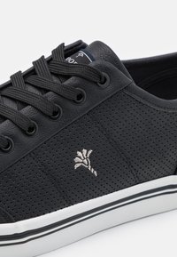 Sorte perforerte lær sneakers med sportstrimler, med en hvit gummisåle aksentuert med svarte og hvite striper og et brodert logo.