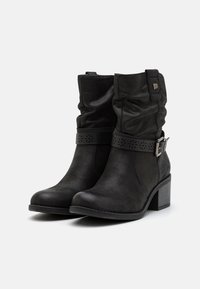 Botas negras hasta el tobillo hechas de suave cuero sintético, con un diseño arrugado, correa decorativa con patrón recortado y un tacón grueso.