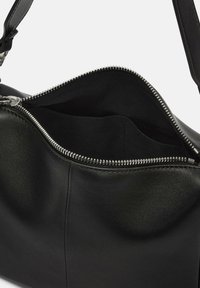 Czarna skórzana torebka o gładkiej teksturze, z metalowym zamkiem błyskawicznym i przestronnym wnętrzem wyłożonym materiałem oraz boczną kieszenią.