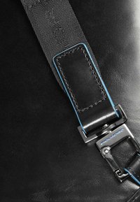 Schwarzes Lederarmband mit blauer Naht, ausgestattet mit einer Metallschließe in Silberoptik. Der Hintergrund ist glatt und matt strukturiert.