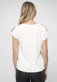 Kortermet hvit t-skjorte med rund hals og mønstrete detaljer på skuldrene, laget av mykt bomullsmateriale.