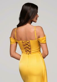 Žluté off-shoulder šaty s přiléhavým siluetem, šněrováním na zádech a bočním zipem. Hladká tkanina s jemným leskem.