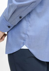 Camicia a maniche lunghe blu, con texture e polsini a bottone, caratterizzata da un orlo leggermente curvo e una sottostrato bianca in contrasto.