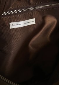 Λευκή ετικέτα ρούχου με μαύρο κείμενο "InWear COPENHAGEN 1969", ραμμένη μέσα σε καφέ ύφασμα κοντά σε μεταλλικό φερμουάρ.