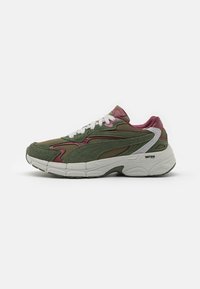 Zapatillas verdes y marrones con parte superior de malla y gamuza, cordones blancos y suela blanca gruesa. Presenta acentos texturizados y un diseño en capas.