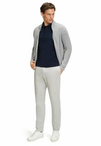 Jasnoszary kardigan w prążki, granatowy polo, szare dresy i białe sneakersy. Strój charakteryzuje się luźnym krojem i swobodnym stylem.