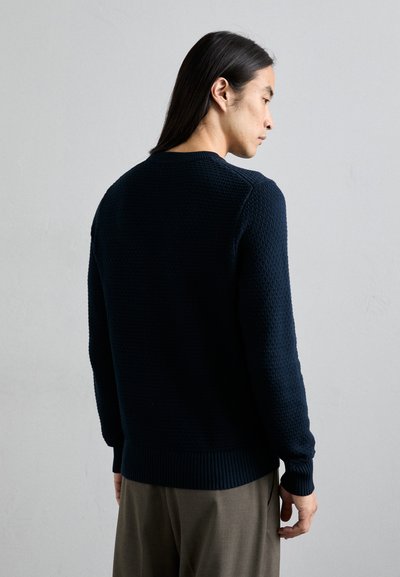 Marineblauer Strickpullover mit einem strukturierten, erhabenen Muster, Rundhalsausschnitt und gerippten Bündchen und Saum. Die Rückseite ist sichtbar und zeigt ein sauberes Design.
