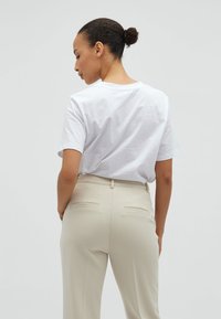 T-shirt bianco in cotone con una vestibilità rilassata e maniche corte, abbinato a pantaloni beige sartoriali con due tasche posteriori.