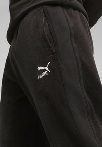 Joggers de forro polar negro con bolsillos laterales, que presentan una superficie texturizada y rayas verticales en contraste. Logo de Puma bordado en la cadera.