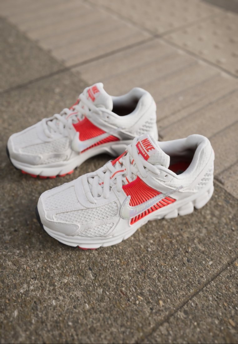 Baskets de sport blanches avec accents rouges, tige en mesh et synthétique, col rembourré, bout rond et semelle texturée. Logo Nike visible sur la languette.