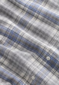 Kostkovaná flanelová látka v šedé, bílé a modré barvě s jemnou texturou; obsahuje knoflíky a vzor křížících se linií.