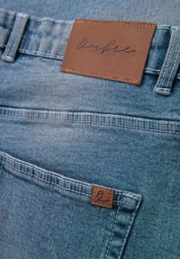 Blå denimjeans med en brun lædermærkat med sort skrift ved linningen over en baglomme med et lille matchende mærke.