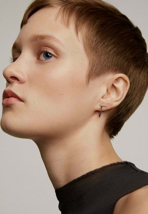 Pendiente de metal negro con un diseño lineal y elegante que presenta pequeños adornos similares a diamantes. El fondo es simple y sutil.