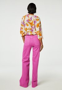 Bloes met bloemen in oranje en paars; roze, brede broek; soepele stof; geraffineerde details bij de kraag en mouwen.